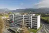Textinsert: Foto Wolfurt, Senderstraße, Außenansicht Wohnbau, parkplatzseitig mit parkenden Autos im Vordergrund und Landschaft im Hintergrund