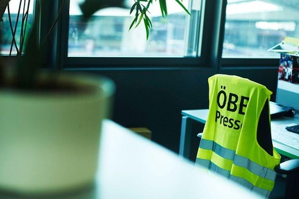 Aufnahme im Büro gemacht eines Arbeitsplatzes. Eine Warnweste hängt über einem Bürostuhl und darauf steht "ÖBB Presse".