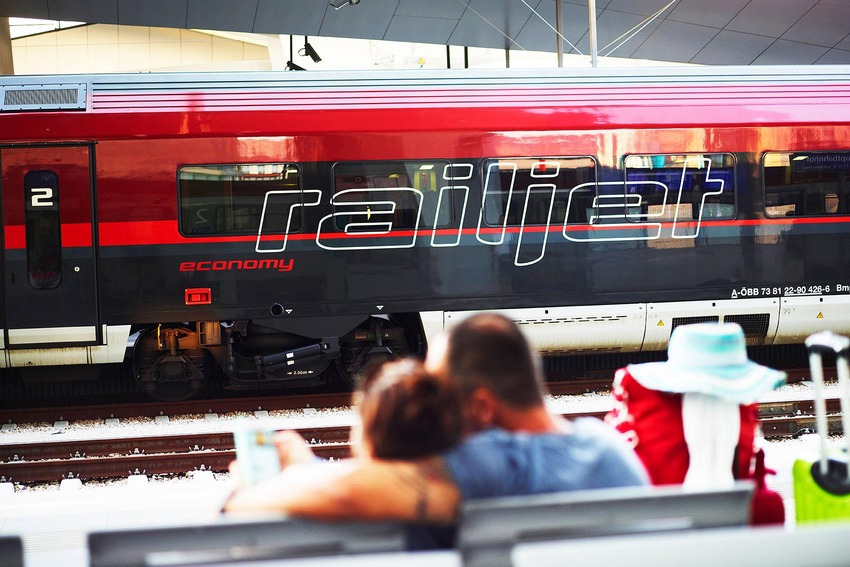 Paar sitzend um umarmend auf Bank, Hintergrund Railjet