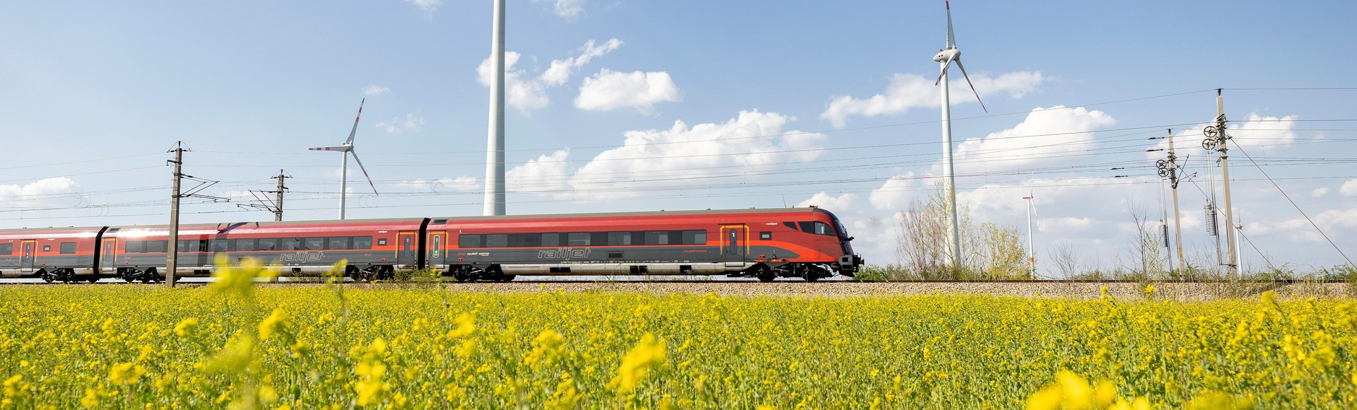 Railjet in sommerlicher Landschaft vor Windrädern