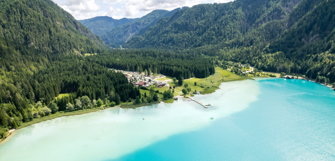 Urlaub am Weissensee: Panoramaaufnahme von einem Weissensee-Strand mit türkisblauen Wasser. 