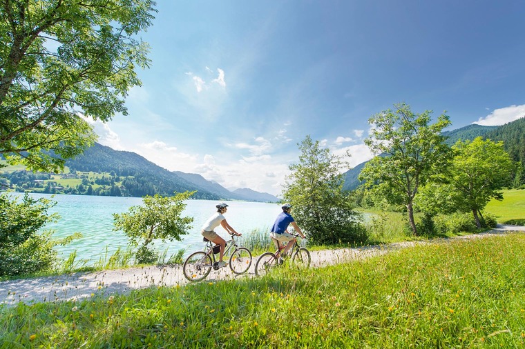 Urlaub am Weissensee: Zwei Radfahrer fahren auf einem Fahrradweg am Ufer des Weissensees. 