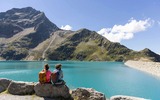 2 Personen sitzen auf einem Stein und schaut auf den See