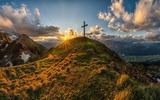 Gipfelkreuz auf einem grünen Berg mit Sonnenstrahlen
