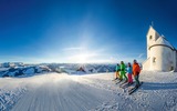 3 Skifahrer vor verschneiter Kapelle