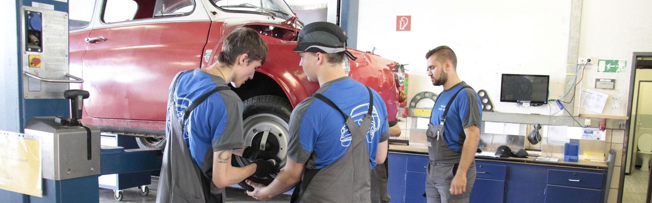 Lehrlinge und Postbus Mitarbeiter stehen in Werkstatt vor einem Oldtimer-Wagen