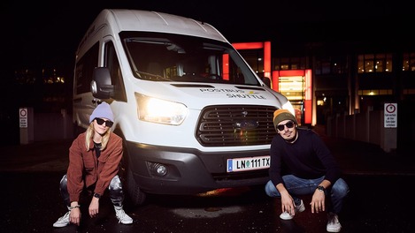 Zwei Personen posen cool vor einem Postbus Shuttle