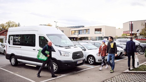 Fahrer und Kundin stehen vor Postbus Shuttle