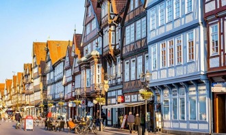 Historische Altstadt von Celle mit farbenfrohen Fachwerkhäusern, kleinen Geschäften und Außengastronomie entlang einer belebten Straße im warmen Abendlicht.<br/>