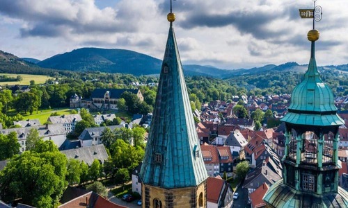 Panoramablick über die Altstadt von Goslar mit roten Ziegeldächern, historischen Gebäuden und markanten Kirchtürmen vor der bewaldeten Mittelgebirgslandschaft des Harzes