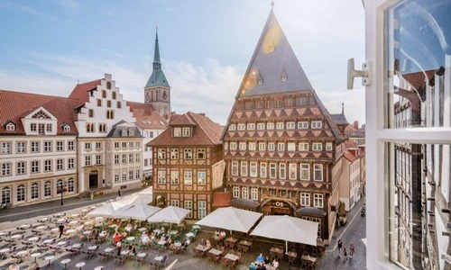 Historischer Marktplatz in Hildesheim mit prächtigen Fachwerkhäusern, Außengastronomie und Blick auf die St.-Andreas-Kirche bei sonnigem Wetter.
