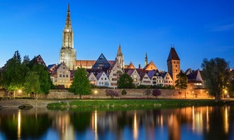 Abendliche Ansicht der Altstadt von Ulm mit dem Münster. Im Vordergrund spiegeln sich die Lichter in der Donau.<br/>
