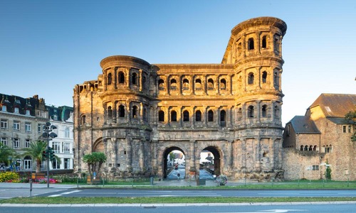 Das römische Stadttor Porta Nigra wird von warmem Abendlicht beleuchtet, umgeben von historischen und modernen Gebäuden