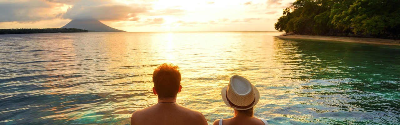 Ein Paar sitzt am Steg und blickt auf den Sonnuntergang am Meer