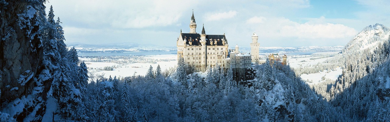 Blick auf bergige Winterlandschaft in der Sonne, in der Mitte Schloss Neuschwanstein