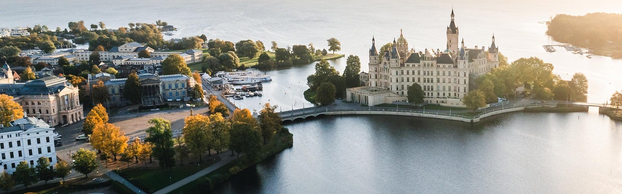 Blick auf das Schweriner Schloss mitten im Wasser im Sonnenuntergang.