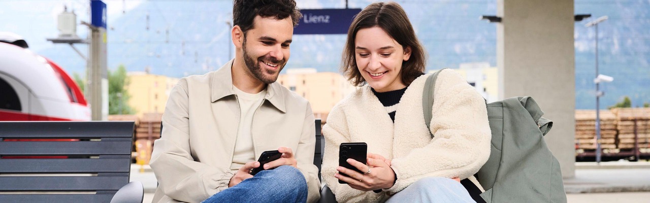 Paar sitzt auf Bahnsteig mit Smartphones in der Hand