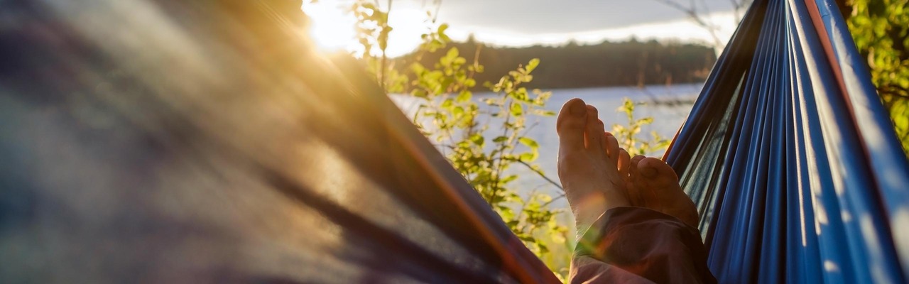 Person lies in a hammock and looks towards the sunset