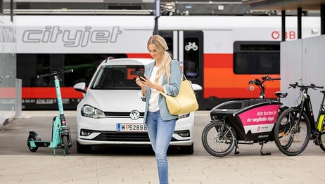 Frau mit Smartphone und Sharing-Fahrzeugen am Bahnsteig