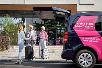 Menschen mit Reisekoffer stehen neben ÖBB Transfer Shuttle