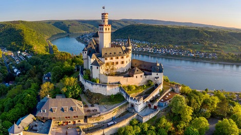 Imposante Burg ragt über eine bergige Waldlandschaft am Fluss hinaus.