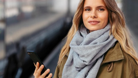 Kundin mit Smartphone steht am Bahnsteig