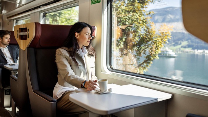 Frau sitzt mit Tasse Kaffee im Railjet und blickt aus dem Fenster