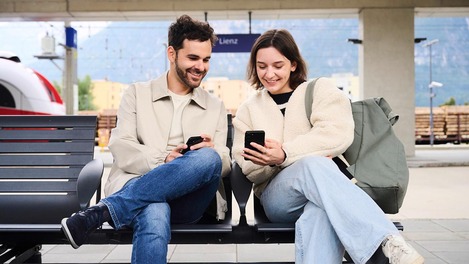 Paar sitzt auf Bahnsteig mit Smartphones in der Hand