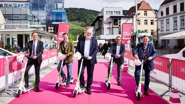 Personen auf E-Scootern auf rotem Teppich