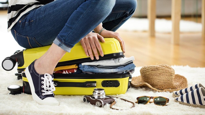 Woman sits on suitcase and tries to close it