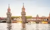 Eine junge Frau und ein Mann fahren bei untergehender Sonne vor der Oberbaumbrücke Stand-up-Paddle auf der Spree.