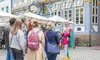 Geführte Stadtführung auf einem gepflasterten Platz vor historischen Fachwerkhäusern; eine kostümierte Figur in bunter Kleidung steht im Mittelpunkt und spricht zu einer kleinen Gruppe von Teilnehmenden, im Hintergrund sind Café‑Tische und Sonnenschirme zu sehen.