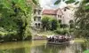 Floßfahrt auf der Oker in Braunschweig mit einer Gruppe von Menschen auf einem bewirteten Floß, umgeben von grüner Uferlandschaft und historischen Villen.