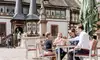 Familie sitzt in einem Straßencafé in der Altstadt von Einbeck, stößt gemeinsam an und genießt die Atmosphäre vor dem historischen Rathaus und einem Brunnen.