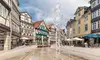 Belebter Stadtplatz in Wolfenbüttel mit Wasserspielen, umgeben von historischen Fachwerkhäusern, Geschäften und Außengastronomie.