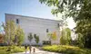 Moderner Museumsbau mit klarer, heller Fassade; ein Weg führt durch eine begrünte Anlage mit jungen Bäumen zum Eingang.<br/>