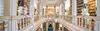Prunkvoller Bibliothekssaal mit umlaufenden Galerien, goldverzierten Balustraden, weißen Büsten und deckenhohen Bücherregalen.<br/>