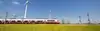 Talent fährt durch Graslandschaft mit Windkraftwerk im Hintergrund