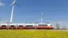 Talent fährt durch Graslandschaft mit Windkraftwerk im Hintergrund