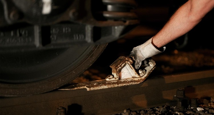 Hand placing a brake shoe against a freight wagon wheel on the track