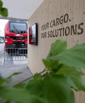 Messestand der Rail Cargo Group auf der Transport Logistic mit roter Lok und Slogan „Your cargo. Our solutions