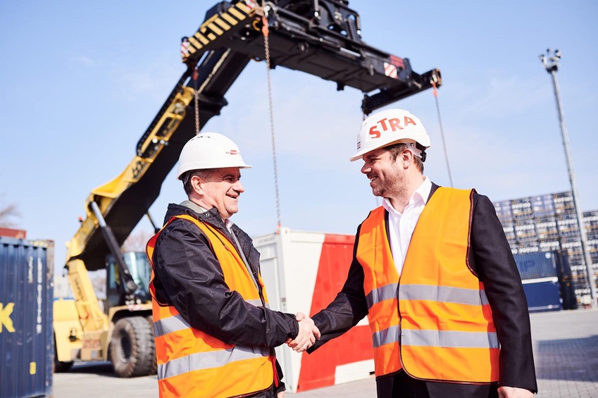 Two men wearing safety helmets and vests shaking hands at a terminal site.