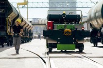 Rail worker walking beside shunting vehicle and freight wagons at a railway yard.