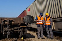 Opening of Terminal Bilk with two employees in safety vests and helmets beside container wagons.