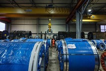 Warehouse San Stino with blue steel coils and a person in orange protective clothing near crane hook