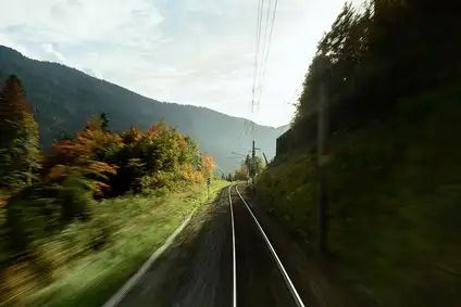Bahnstrecke durch grüne Hügellandschaft, Blick aus fahrendem Zug.