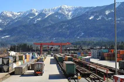 Containerterminal Villach Süd mit gestapelten Containern, Güterwagen und Portalkran vor alpiner Bergkulisse