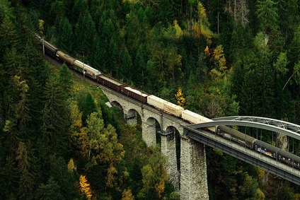 Ein Güterzug überquert ein Viadukt, eingebettet in eine grüne Waldlandschaft.