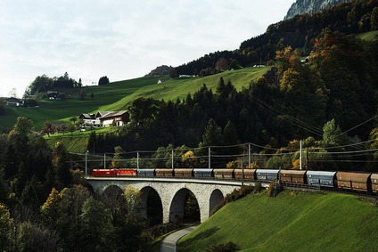 A freight train with an ÖBB locomotive crosses a viaduct in a green hilly landscape.