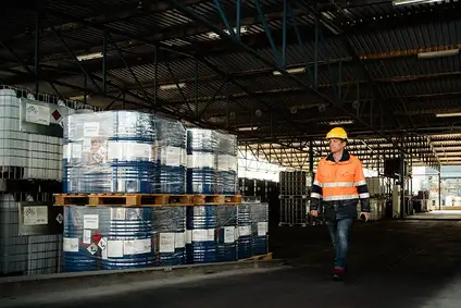 Arbeiter in Schutzkleidung geht an gestapelten Chemiefässern im Lager Krems vorbei.